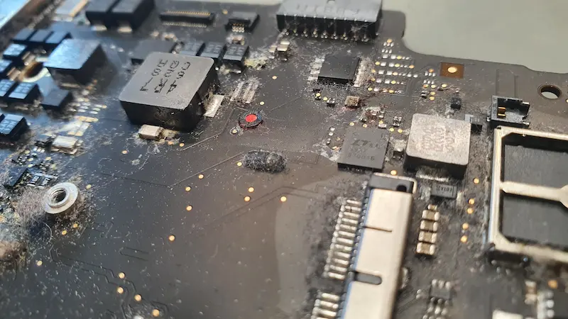 Zalana płyta główna MacBooka po kontakcie z cieczą, widoczne ślady korozji i zabrudzeń na podzespołach elektronicznych. Specjalistyczna naprawa laptopów po zalaniu we Wrocławiu.