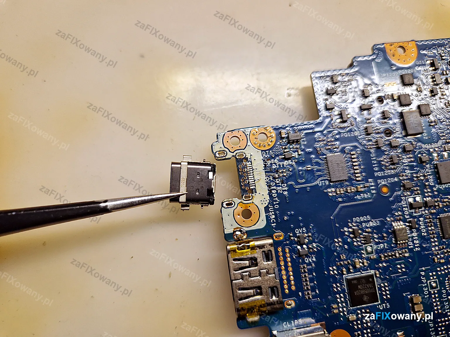 Gniazdo USB-C trzymane pęsetą przy płycie głównej laptopa ASUS ZenBook