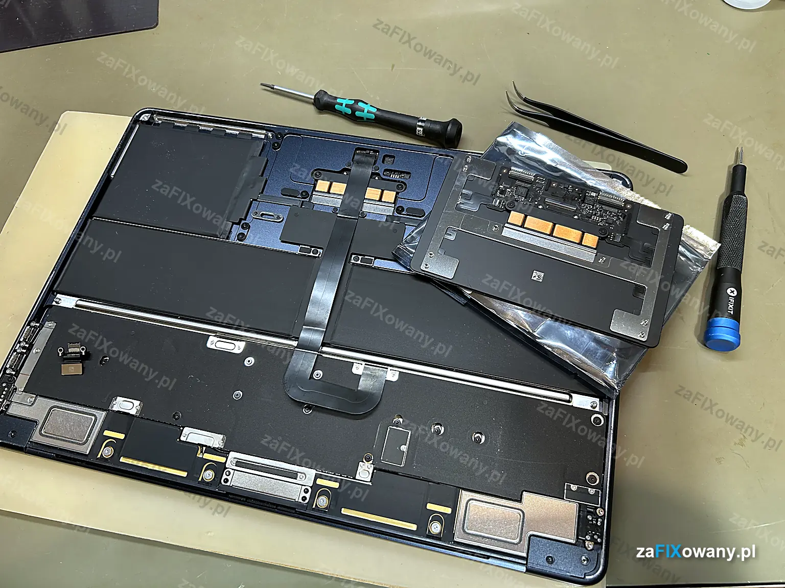 Otwarty MacBook Air M2 na stanowisku serwisowym, obok nowy gładzik w worku antystatycznym