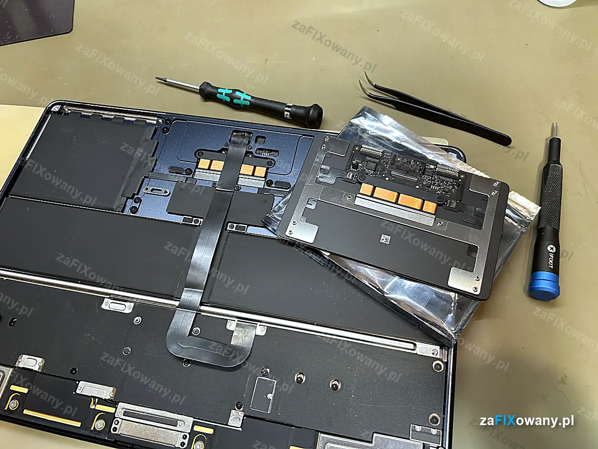 Nowy gładzik Force Touch do MacBooka Air M2 od spodu, z silniczkiem haptycznym, obok otwarty laptop