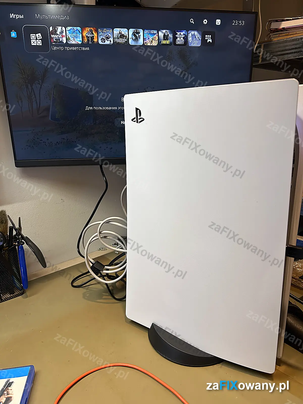 PS5 po naprawie stoi pionowo, na monitorze menu główne konsoli